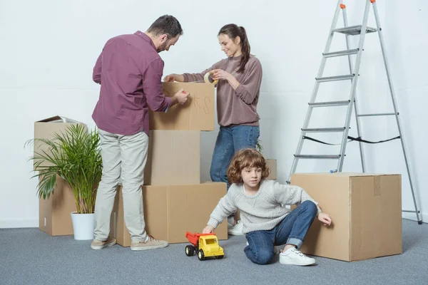 Родители упаковывают коробки и сын играет с игрушечным автомобилем во время переезда — стоковое фото
