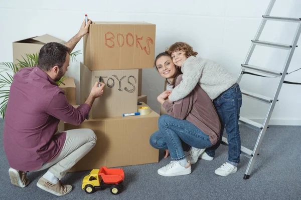 Familia feliz con un niño firmando cajas mientras se muda a un nuevo hogar - foto de stock