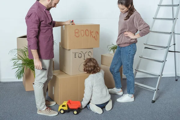 Recortado tiro de feliz familia con un niño firmar cajas mientras se muda a casa nueva - foto de stock