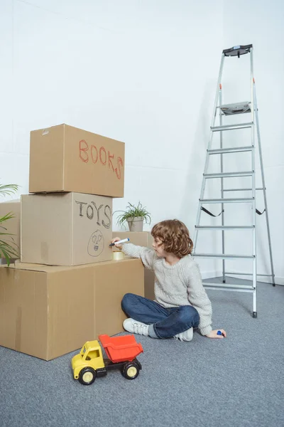 Mignon petit garçon chantant boîtes en carton tout en déménageant à la maison — Photo de stock