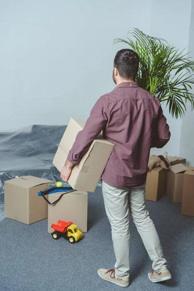 Back view of man holding cardboard box while moving in new house — Stock Photo