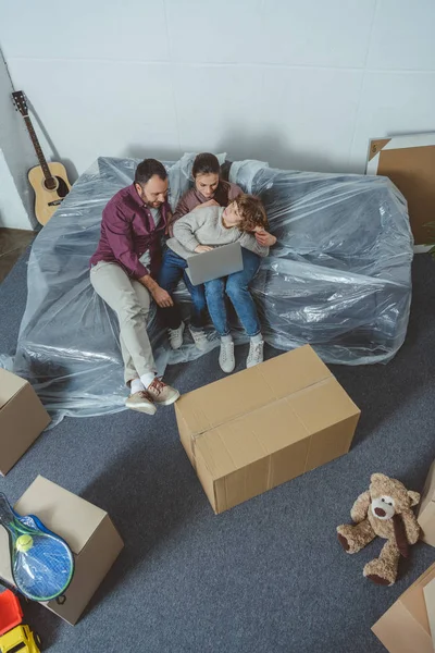 Visão de alto ângulo da família com uma criança usando laptop enquanto se move em novo apartamento — Fotografia de Stock
