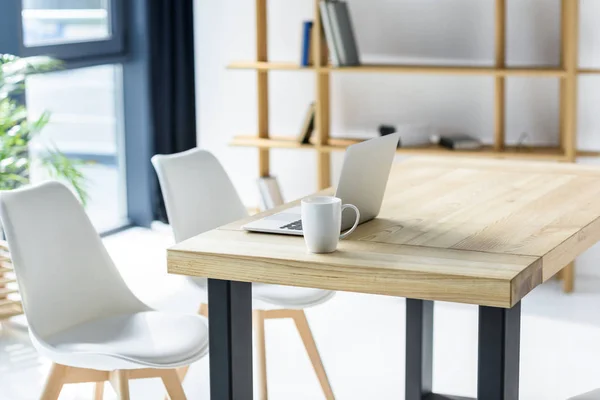 Ordinateur portable et tasse de café sur la table dans le bureau moderne — Photo de stock