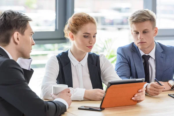 Equipo exitoso discutiendo proyecto por tableta en la oficina moderna - foto de stock