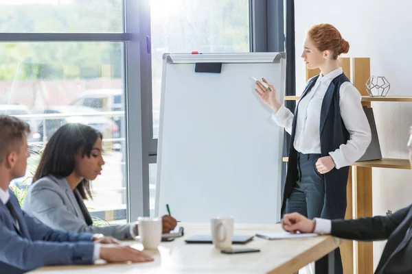 Femme d'affaires confiante présentant son idée par tableau à feuilles mobiles à ses collègues dans le bureau moderne — Photo de stock