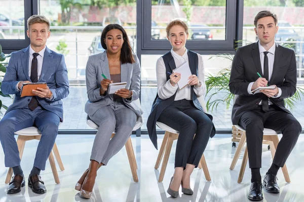 Hommes d'affaires et femmes d'affaires avec bloc-notes à l'écoute de la présentation dans le bureau moderne — Photo de stock