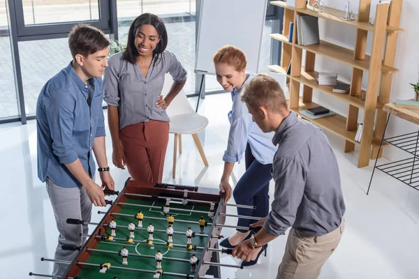 Equipo de compañeros de trabajo jugando futbolín en oficina moderna - foto de stock