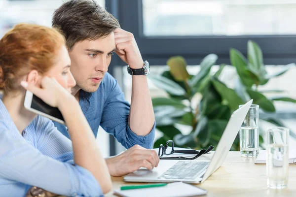 Pensativo hombre de negocios y mujer de negocios que trabaja por computadora portátil en la oficina moderna - foto de stock