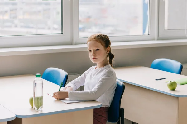 Красива маленька школярка пише в класі в школі — стокове фото