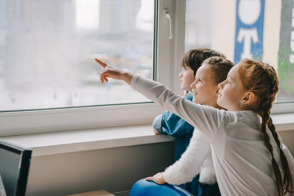 Adoráveis escolares olhando para a janela juntos na sala de aula e apontando para algum lugar — Fotografia de Stock