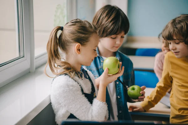 Teen schoolchildren eating apples together at classroom — Stock Photo