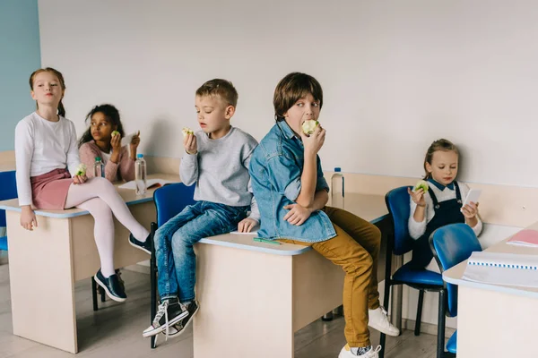Escolares que comem maçãs na sala de aula enquanto descansam — Stock Photo