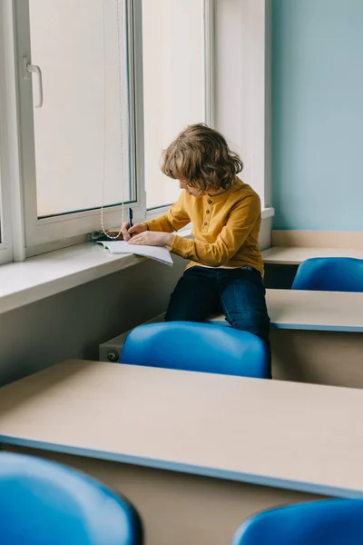 Entzückendes kleines Kind schreibt Hausaufgaben auf der Fensterbank — Stockfoto