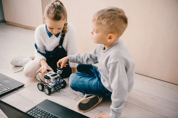 Schüler sitzen mit Roboter und Laptop auf dem Boden — Stockfoto