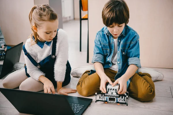 Focused kids programming robot while sitting on floor at machinery class — Stock Photo