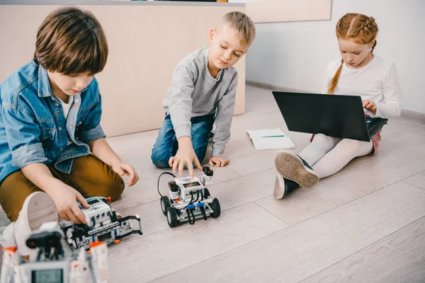 Little kids sitting on floor at stem education class with robots and laptop — Stock Photo