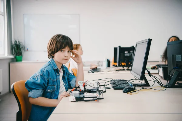 Teenie-Kind schaut in Kamera, während es im Maschinenkurs einen Roboter programmiert — Stockfoto