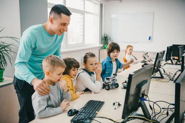 Happy young teacher helping his teen students with diy robot on stem education class — Stock Photo