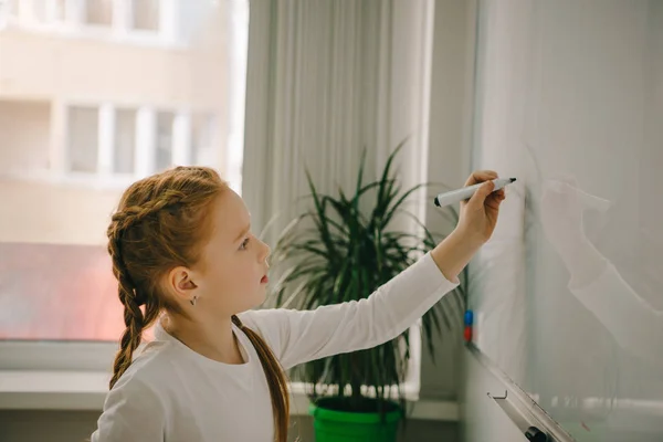 Pequena estudante feliz escrevendo no quadro branco — Fotografia de Stock
