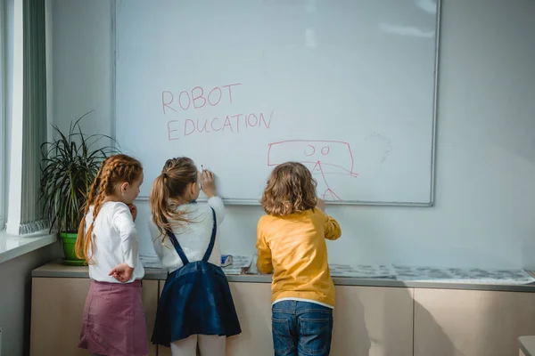 Visão traseira de crianças escrevendo e desenho robô sinais de educação no quadro branco — Fotografia de Stock