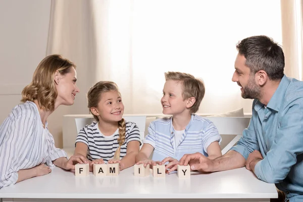 Familia sonriente sentada en la mesa - foto de stock