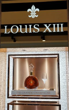 DUBAI, UAE - November 14, 2019: A bottle of Louis XIII By Remy Martin Cognac and a glass on a branded display showcase. clipart