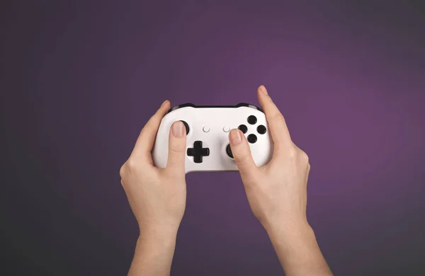 Tangan memegang gamepad putih terhadap latar belakang ungu — Stok Foto