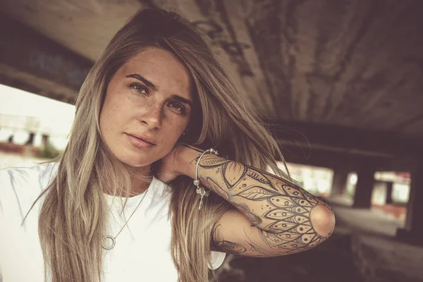 Portrait of a young beautiful blonde in a white T-shirt and with tattoos, looks at the camera, close-up — Stock Photo, Image