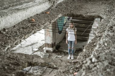 Ocak ızgarası ile görüntüleyin. Beyaz bir T-shirt ve jeans içinde yalnız bir kız harap bir ev kalıntıları üzerinde duruyor. Üzgün ifade, trajik bir atmosfer.