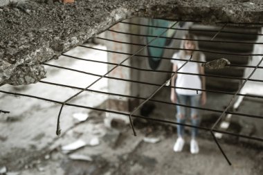 Ocak ızgarası ile görüntüleyin. Beyaz bir T-shirt ve jeans içinde yalnız bir kız harap bir ev kalıntıları üzerinde duruyor. Üzgün ifade, trajik bir atmosfer.