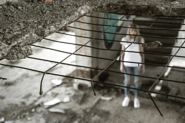 Ocak ızgarası ile görüntüleyin. Beyaz bir T-shirt ve jeans içinde yalnız bir kız harap bir ev kalıntıları üzerinde duruyor. Üzgün ifade, trajik bir atmosfer.
