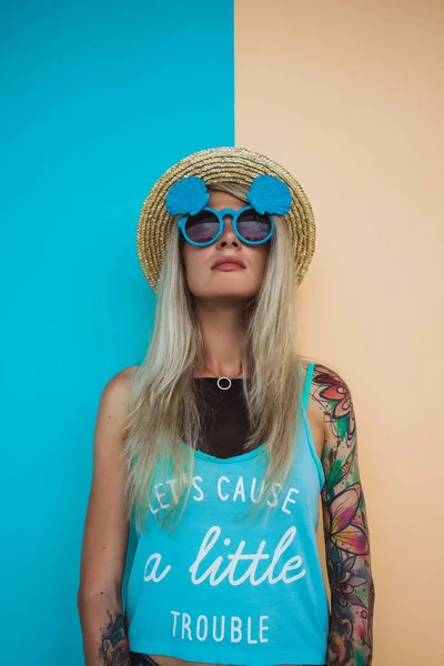 Vacker ung kvinna hipster med en tatuering i solglasögon och en hatt på en ljust färgad bakgrund. Beach stil — Stockfoto