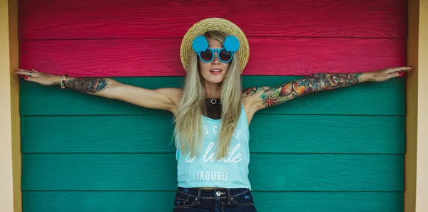 Mulher bonita hipster com uma tatuagem em óculos de sol e um chapéu em um fundo colorido brilhante. Estilo praia — Fotografia de Stock