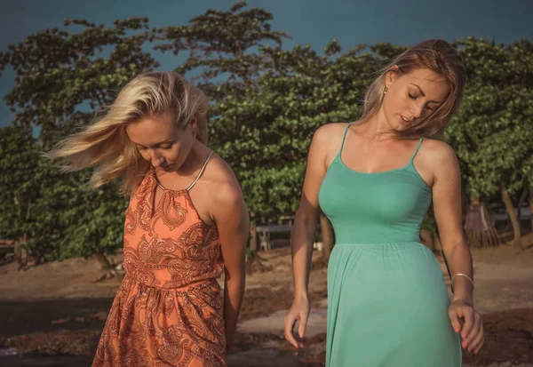 Två mode modeller poserar i röda och turkosa klänningar i strålar solen på en tropisk strand — Stockfoto