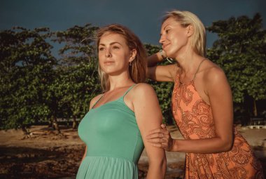 Tropikal bir plajda güneşin ışınları kırmızı ve turkuaz kıyafetlerle poz iki moda modelleri