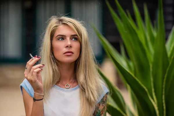 Mooi blond meisje rookt een sigaret. Womens handen met een tatoeage. Stedelijke mode — Stockfoto