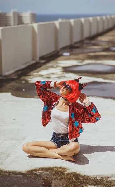 Beautiful girl devil sitting on city background near the puddle with his reflection. In anticipation of Halloween. Portrait. Wears black sunglasses — Stock Photo, Image