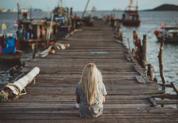 Hipster meisje zit op houten pier in de stralen van de ondergaande zon. Een vakantie in Thailand. Terug naar de camera. Vakantie in Azië. — Stockfoto