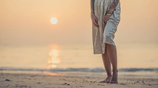 在清晨海滩的女性脚特写。年轻现代女孩在一条长的裙子站立在波光粼粼的水 — 图库照片