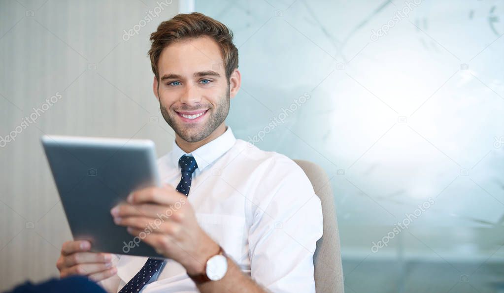 Portrait of a handsome young business entrepreneur smiling at the camera while holding a digital tablet