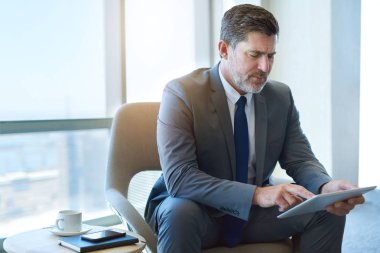 Mature executive in a corporate suit, using a digital tablet while sitting in a business lounge