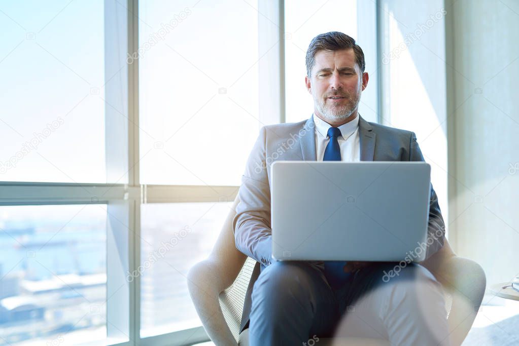Mature corporate business executive sitting in a modern office space working on his laptop 