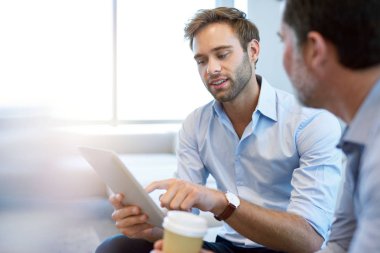 Yakışıklı genç bir iş adamı, olgun bir meslektaşıyla fikirleri tartışırken dijital tablet kullanıyor.