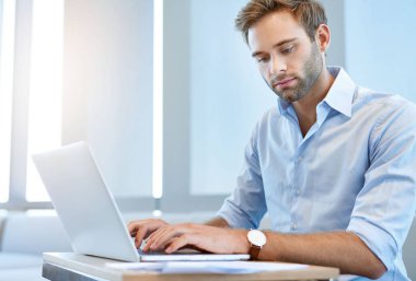 Yakışıklı genç işletme yöneticisi bazı evrak işlerini halletmek için dizüstü bilgisayarını kullanıyor.