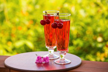 Kiraz ile iki bardak kırmızı bir içecek ile dolu. Kokteyl bokeh yeşil zemin üzerine bir bardak şampanya. İki karanfil masanın üzerinde. Metin için yeterince boş alana.