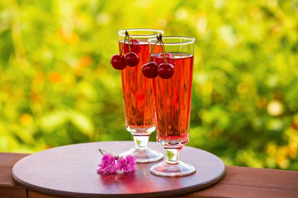 Kiraz ile iki bardak kırmızı bir içecek ile dolu. Kokteyl bokeh yeşil zemin üzerine bir bardak şampanya. İki karanfil masanın üzerinde. Metin için yeterince boş alana.