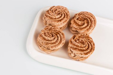 Dört tane tarçın ve çikolata serpiştirilmiş marşmelov beyaz dikdörtgen bir tabakta yatıyor. Üst görünüm, beyaz arkaplan.