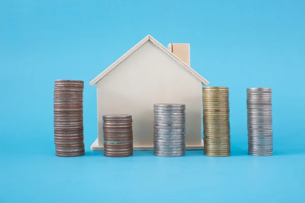 Stapel van munten en houten huis symbool op blauwe zachte achtergrond — Stockfoto