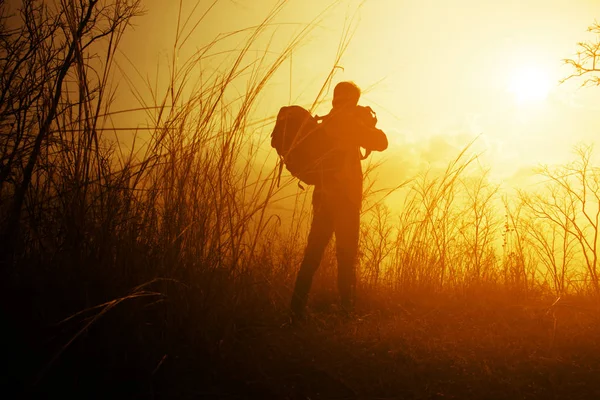 Traveler with backpack taking photo on the mountain at sunset