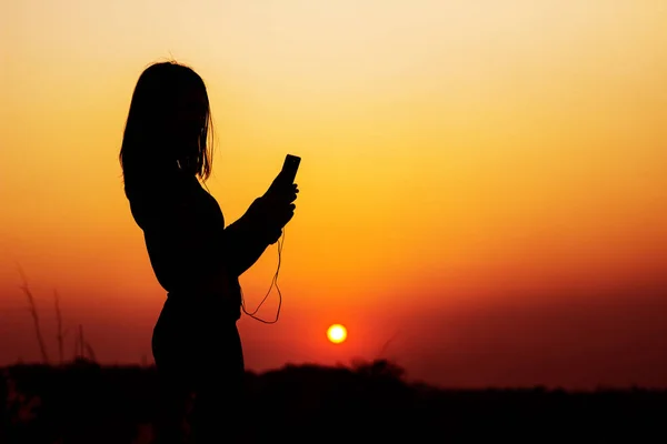 Silueta mujer tomando fotos de la puesta del sol mediante el uso de teléfono inteligente — Foto de Stock